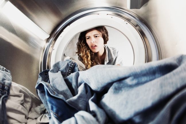 Pretty woman pulling face at laundry in drier